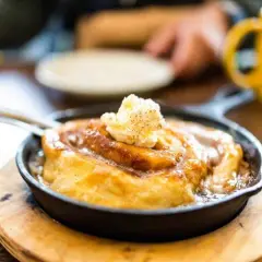 Ein warmer Zimtschnecken-Auflauf in einer Gusseisenpfanne, gekrönt mit Butter. Perfekt, um den Zimtgeschmack zu neutralisieren und den Genuss zu steigern.