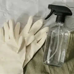 Para gumowych rękawiczek i butelka z atomizerem na zielonym tle.