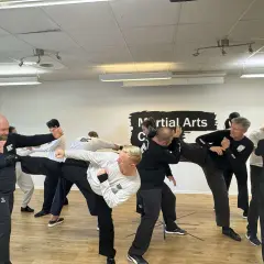 Män tränar wing chun i en lokal. En man utför en hög spark medan andra övar försvar.