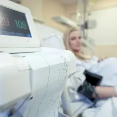 Monitor KTG z wydrukiem zapisu i ciężarną w tle.