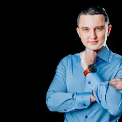 Mężczyzna w niebieskiej koszuli, z rękami skrzyżowanymi na piersi, podczas sesji biznesowej.