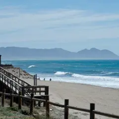 Un día perfecto para un paseo marítimo en Retamar. La arena dorada, el mar azul y las montañas de fondo crean un paisaje idílico.