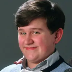 Uśmiechnięty Dudley Dursley, kuzyn Harry'ego Pottera, w niebieskim swetrze.