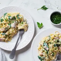 Dwa talerze spaghetti z kremowym sosem, szpinakiem i kawałkami tuńczyka z puszki, posypane natką pietruszki.