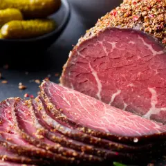 Pokrojone plastry pastrami, przyprawione pieprzem, obok ogórków konserwowych. Zastanawiasz się pastrami co to? To aromatyczne, peklowane i wędzone mięso wołowe.