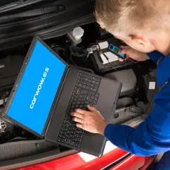 Mecánico revisa el motor de un coche con un portátil y un dispositivo de diagnóstico. El **stage** de la revisión es crucial para el **significado** del buen funcionamiento.