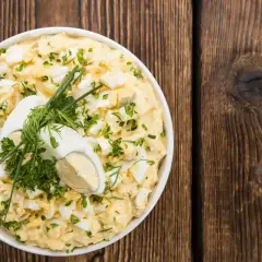 Insalata cremosa con uova di quaglia sode, erbe fresche e un uovo intero a metà come guarnizione, servita in una ciotola bianca su un tavolo di legno rustico.