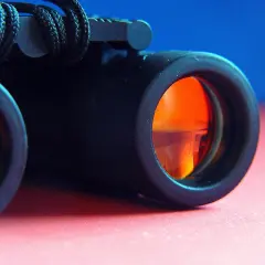 Primo piano di un binocolo nero con lenti arancioni, pronto per esplorare il mondo.