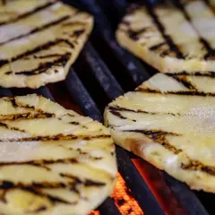 Tranches d'ananas barbecue grillées, avec des marques de cuisson foncées sur fond de braises rougeoyantes.