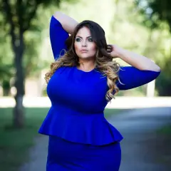 Kobieta w niebieskiej sukience z baskinką, prezentująca modne bluzki dla puszystych.