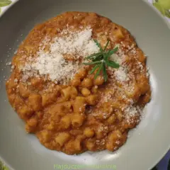 Pyszny makaron z ciecierzycy w sosie pomidorowym, posypany parmezanem i gałązką rozmarynu.