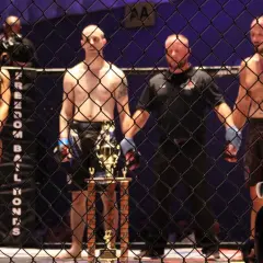 Ring girls i zawodnicy MMA czekają na rozpoczęcie freak fight. Trofeum lśni w blasku reflektorów.