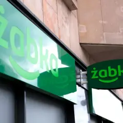 Zielony neon z logo Żabki. Zastanawiasz się, od ilu lat można pracować w Żabce? Odpowiedź znajdziesz w tym sklepie.