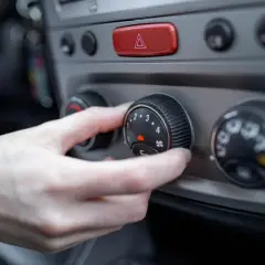 Mano ajustando el control del aire acondicionado a modo frio. El dial muestra números del 1 al 4 y un icono de ventilador.