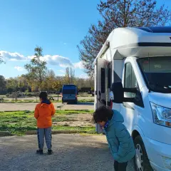 Deux enfants devant un camping-car Challenger, en route pour une aventure dans le sud de la France. Le soleil brille, les arbres perdent leurs feuilles.