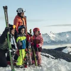 En glad familj njuter av sin skidresa i Alperna. Barnen ler mot kameran med skidor och stavar, redo för äventyr i snön.