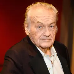 Jerzy Skolimowski, reżyser znany z wyrazistych filmów, na tle czerwonej kurtyny.