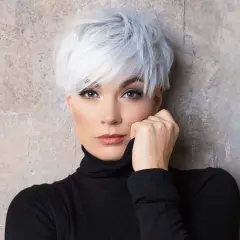 Kobieta z krótkimi, kręconymi, białymi włosami w czarnym golfie, opierająca dłoń o twarz.