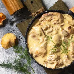 Kremowy sos grzybowy z kawałkami mięsa w czarnej patelni, ozdobiony koperkiem.