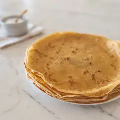 Pile de crêpes dorées, parfaites pour une recette crêpe moelleuse. Un petit bol de sucre est à côté.