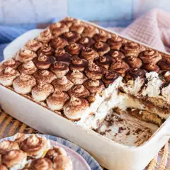 Cremiges, veganes Tiramisu ohne Alkohol, bestäubt mit Kakao. Ein Stück wurde bereits entnommen, was die Schichten aus Creme und Löffelbiskuits zeigt.