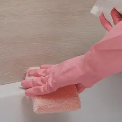 Main rose, une éponge rose nettoie le joint silicone jauni de la baignoire.