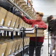 Mitarbeiter im Lager führen pick & pack aus, greifen Kartons aus Regalen und legen sie in Wagen.