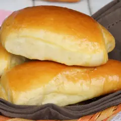 Deliziosi panini al latte dorati, morbidi e invitanti, serviti in un cestino foderato con un tovagliolo marrone.