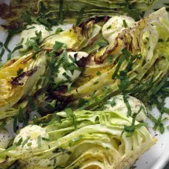 Ugnsbakad vitkål, skuren i klyftor, serverad med en krämig dressing och färska örter. En enkel men smakrik rätt.