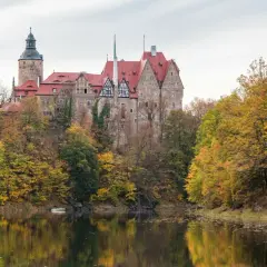 Zamek Kliczków w jesiennej odsłonie, idealne miejsce na jednodniowy wypad w Polsce. Otoczony kolorowymi drzewami, odbija się w spokojnej tafli wody.