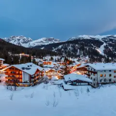 Paesaggio innevato di Madonna di Campiglio al crepuscolo. Hotel illuminati e montagne sullo sfondo, un invito a scoprire cosa vedere.