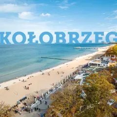 Widok na plażę w Kołobrzegu z ludźmi, budynkami i morzem.