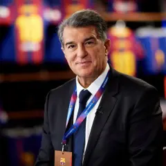 Prezes FC Barcelona, Joan Laporta, w garniturze, z identyfikatorem klubu na szyi, na tle klubowych koszulek.