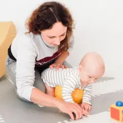 Mama wspiera 2-miesięczne dziecko w pierwszych próbach raczkowania. Zabawy z maluszkiem na macie.