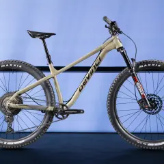 A tan Devinci Kobain mountain bike with Maxxis tires and a Marzocchi Bomber fork, ready for any trail.