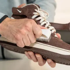 Man limpiando zapatillas de ante marrón con un cepillo blanco. Paso a paso para saber como limpiar zapatillas de ante y dejarlas como nuevas.