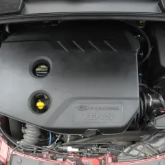 Silnik Duratorq TDCI w Fordzie Focus MK3 1.6. Widoczna czarna osłona silnika z napisem, zbiornik płynu chłodniczego i inne elementy komory silnika.