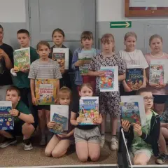 Grupa dzieci i dorosła kobieta pozują do zdjęcia, trzymając w rękach książki.