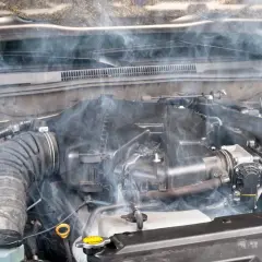 Humo blanco emana del motor de un coche, indicando posible agua en el motor.