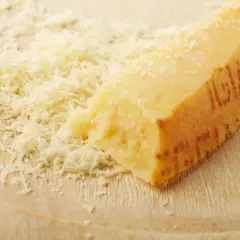 Ein Stück Parmesan mit geriebenem Käse daneben. Die Rinde ist deutlich geprägt und zeigt, dass die **Parmesanrinde essbar** ist.