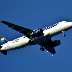 Samolot linii nouvelair z wysuniętym podwoziem wznosi się na tle błękitnego nieba.