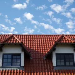 Czerwona dachówka, czy to betonowa czy ceramiczna, pokrywa dach domu z dwoma lukarnami.