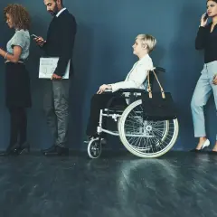 Różne rodzaje niepełnosprawności w kolejce do pracy: osoba na wózku inwalidzkim i inni kandydaci.