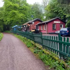 Der Weg zum Bahnhof Burgholz führt vorbei an einer roten Gaststätte mit grünen Zäunen und Autos.