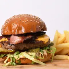 Apetyczny burger wołowy z bekonem, serem, warzywami i frytkami na desce.