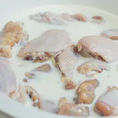 Kawałki kurczaka w mleku, przygotowane do marynowania. To sekret najlepszej marynaty do piersi z kurczaka, która sprawi, że mięso będzie soczyste i delikatne.