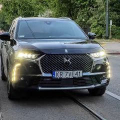 Czarny DS 7 z włączonymi światłami dziennymi stoi na torach tramwajowych.