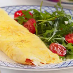 Tortilla francesa rellena, dorada y esponjosa, servida con una fresca ensalada de rúcula y tomates cherry. Un bocado delicioso y saludable.