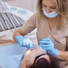 Dentystka bada pacjentkę, która skarży się na krwawiące dziąsła. W gabinecie stomatologicznym widać narzędzia dentystyczne.