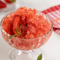 Sorbet truskawkowy w pucharku, ozdobiony plasterkiem truskawki i miętą.